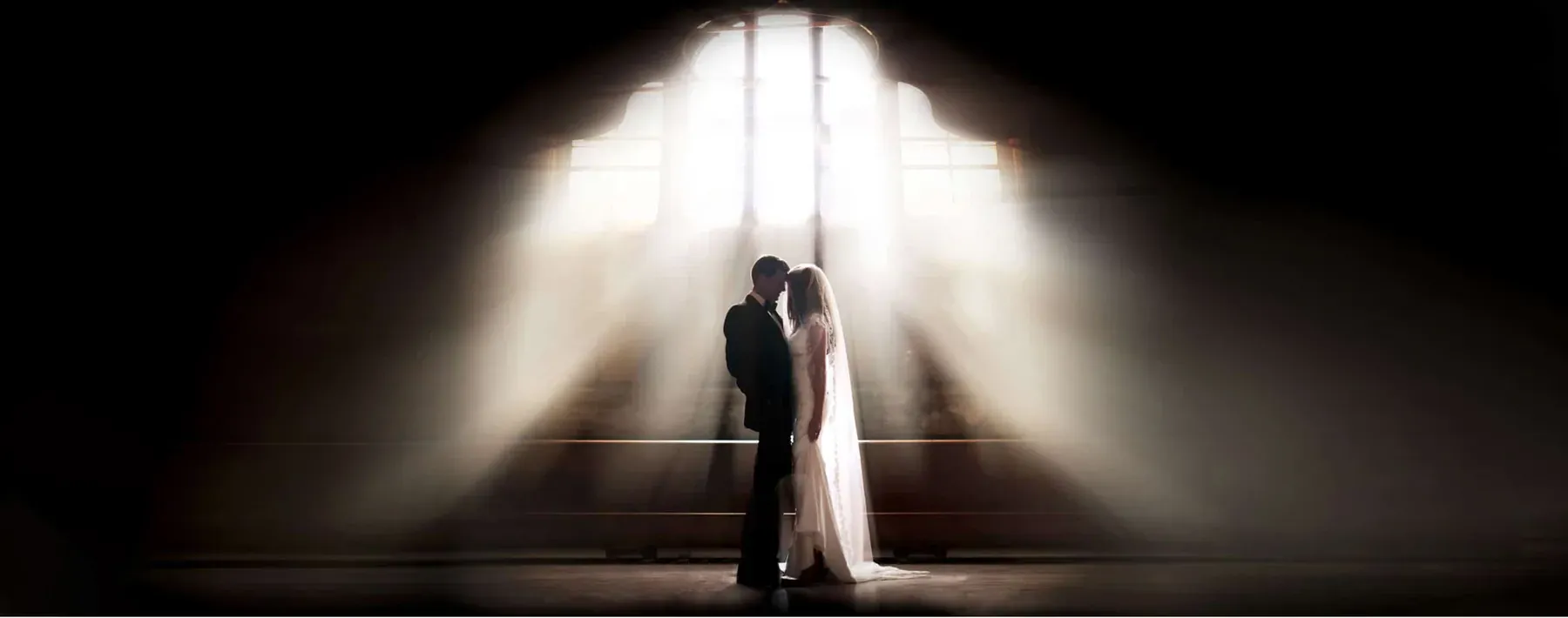 Silhouetted bride and groom beneath dramatic beams of light