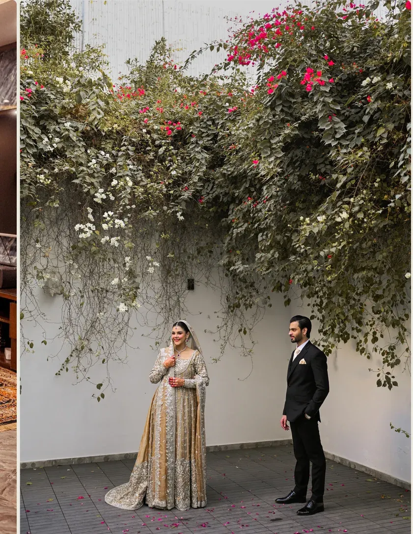 Bride and groom posing together outdoors beside greenery