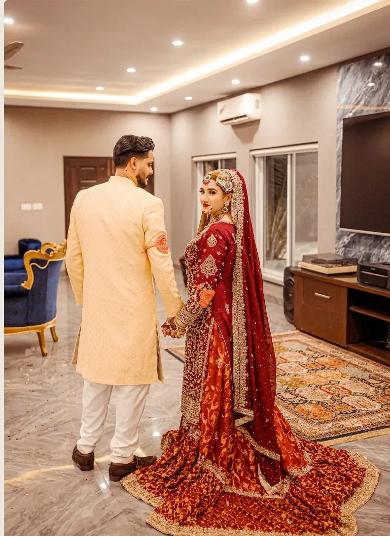 Bride in red bridal attire standing beside groom in a wedding portrait
