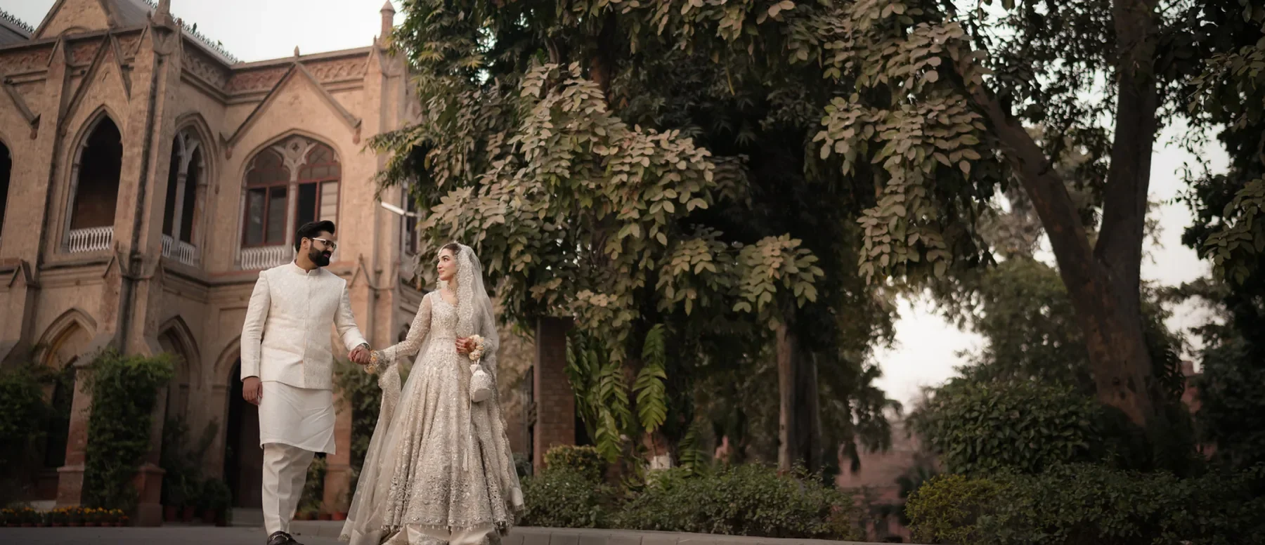 Bride and groom walking together by a heritage building — from the MS Studio wedding brochure